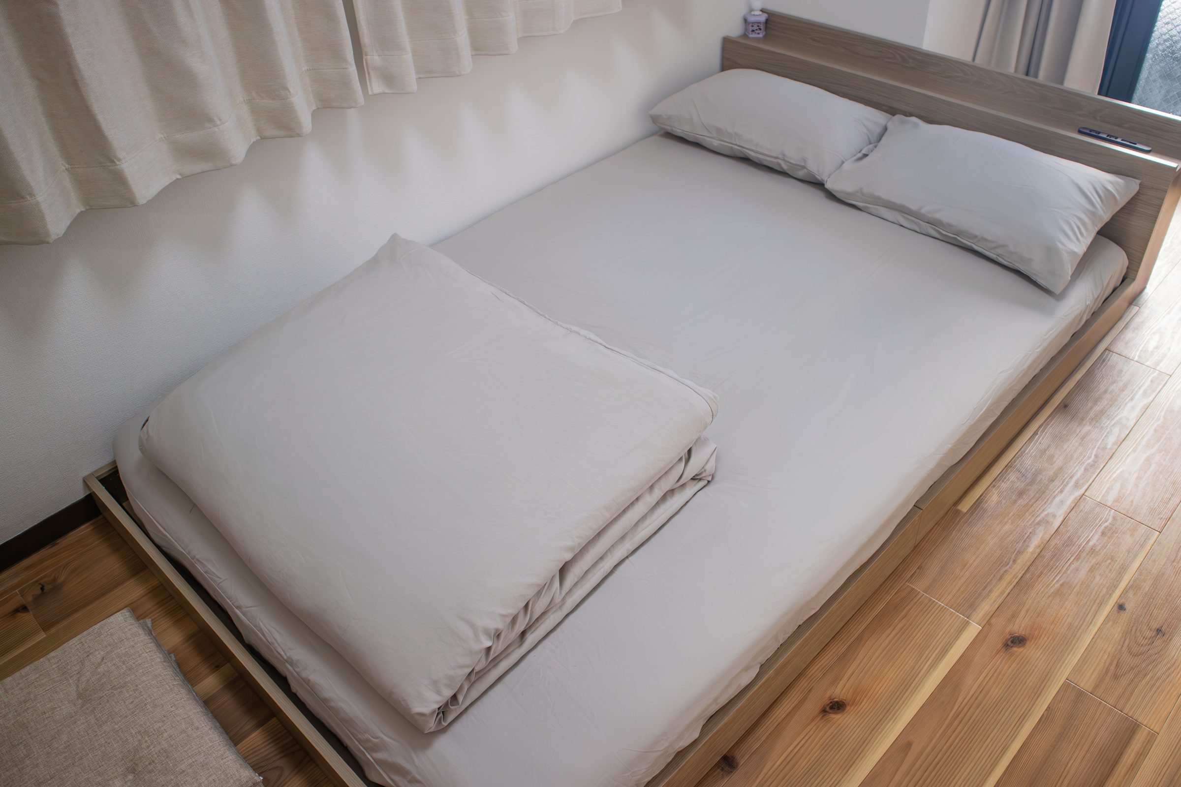 Double bed with white linens in a room with wooden floors.